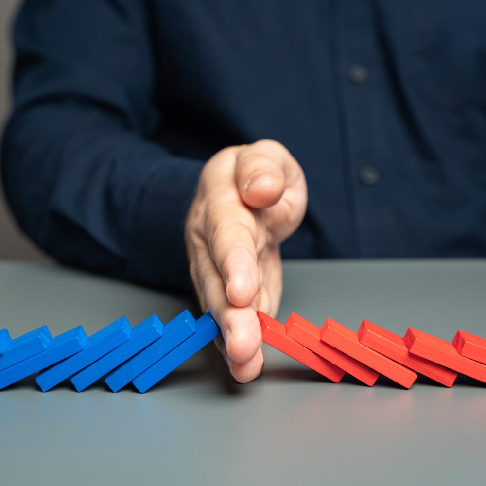 A man stops two domino chains from colliding. The concept of stopping a conflict and preventing further escalation. Elections and confrontation of the parties. Mentoring. Find points of compromise.