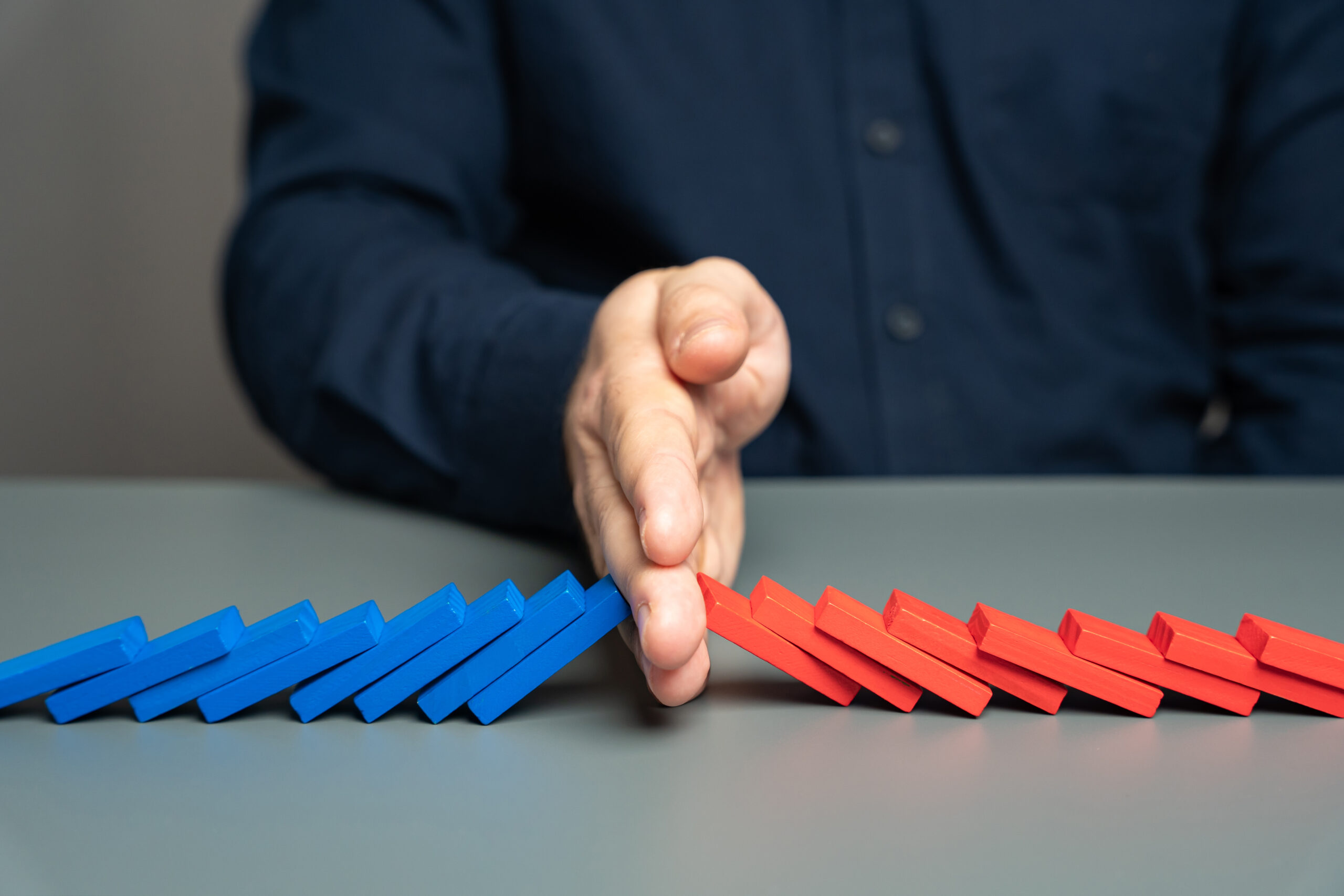 A man stops two domino chains from colliding. The concept of stopping a conflict and preventing further escalation. Elections and confrontation of the parties. Mentoring. Find points of compromise. A man stops two domino chains from colliding. The concept of stopping a conflict and preventing further escalation. Elections and confrontation of the parties. Mentoring. Find points of compromise.
